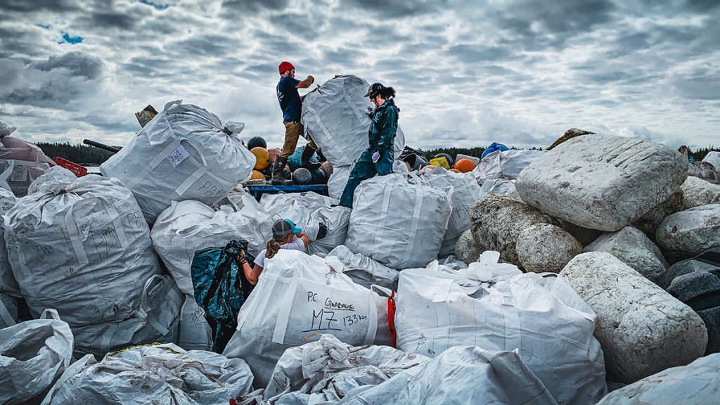 Team members stand on a mountain of garbage bags as they sort through trash on the barge